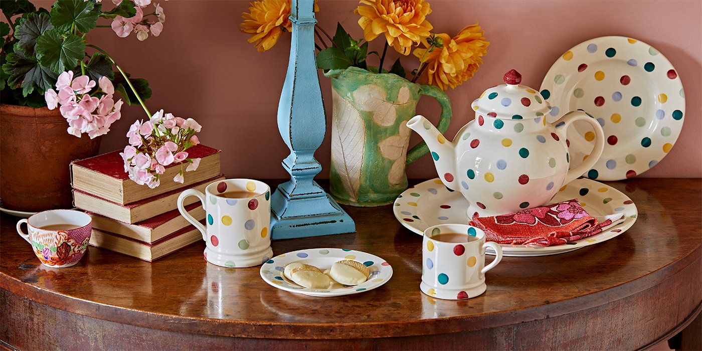 Colourful polka dot tea pot and a matching personalised name mug placed on a wooden table. Bright and colourful tableware inspiration.